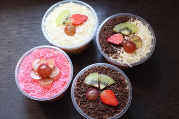 fresh fruit salad of melon, grape, strawberry, kiwi dressed with yoghurt  chopped Apple. cheese and fruits for upper topping. served in a square plastic on wooden tray. selective focus