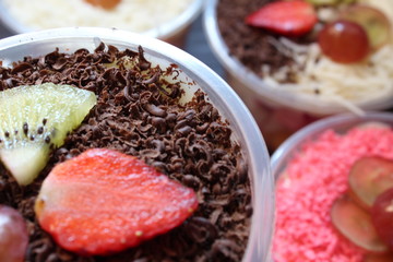 fresh fruit salad of melon, grape, strawberry, kiwi dressed with yoghurt  chopped Apple. cheese and fruits for upper topping. served in a square plastic on wooden tray. selective focus