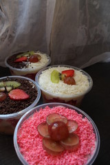 fresh fruit salad of melon, grape, strawberry, kiwi dressed with yoghurt  chopped Apple. cheese and fruits for upper topping. served in a square plastic on wooden tray. selective focus