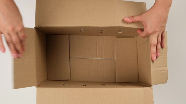 female hand opens brown cardboard box and fills with white filler for safe transportation, top view, moving concept