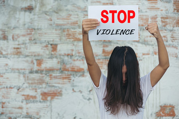 A young woman in a white shirt holding a notebook with the words stop violence.