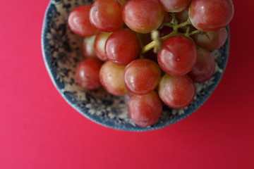 Directly Above View A Bowl Of Red Grapes Against Pink Background