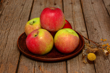 Ripe red apples on plate with dry flower on wooden table. Harvest of ripe apples. Church celebration of the apple feast day. harvest concept 