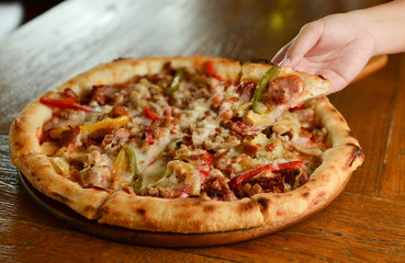 a woman hand pick up the pizza on wooden table