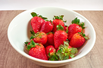 Red and juicy strawberries in a white bowl on a wooden board and white background