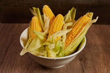 Various fresh Corn on the cob in a white bowl on the table