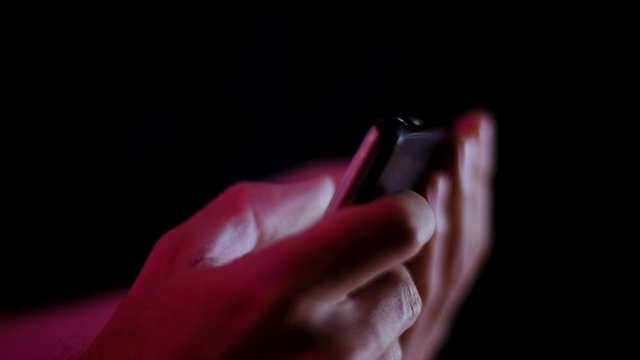Thumb on a smartphone while a video plays in landscape close up in a dark room side profile