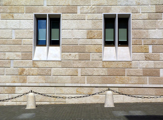 stone facade detail with narrow vertical glass windows. black steel chain barrier attached to stone...