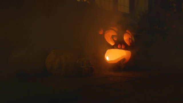 1 carved lit pumpkin outside the front of a house Halloween with smoke slow motion