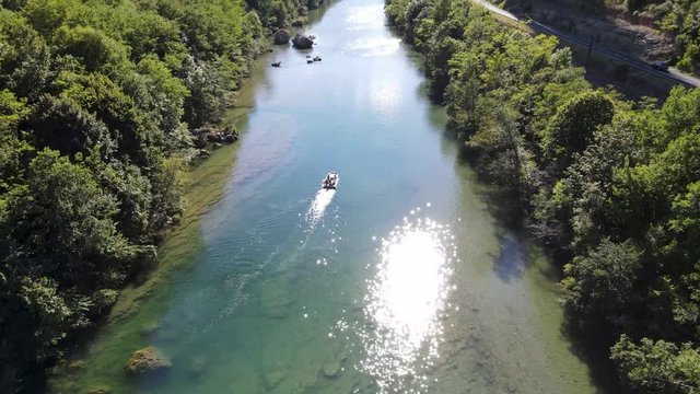 Aerial shot following a boat up the green river with car passing by on the road and tall viaduct in the back. Small boat moving up the river with gorgeous reveal of viaduct and beautiful river valley.