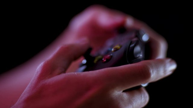 Playing video games in a darkened room with a black background close up on a controller buttons playing quickly soft focus