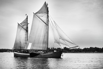 An elegant two-masted gaff schooner (tall ship) sailing near the lighthouse, close-up. Riga bay, Ba;tic sea, Latvia. History, transportation, sport, recreation, cruise, regatta.  Black and white image