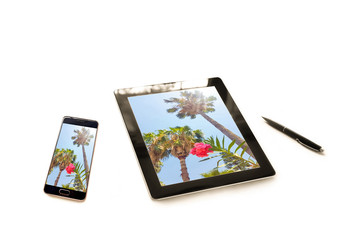 Tablet pc and smartphone with similar screen wallpapers, palms and flowers view with sun light flash effect
