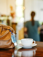 Mini alcohol gel bottle to kill Corona Virus(Covid-19) hang on a brown leather shoulder bag with hot coffee on table in cafe.New normal lifestyle.Health care concept.Selective focus on alcohol gel