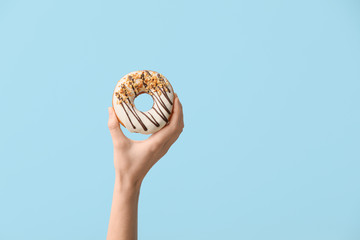 Hand with tasty donut on color background