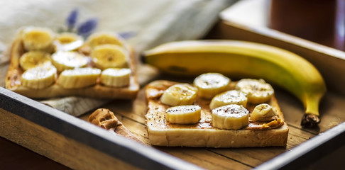 two peanut butter sandwiches and banana on wooden tray