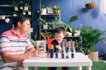 Parent sitting homeschooling with little kid, Father and son having fun preparing easy science...