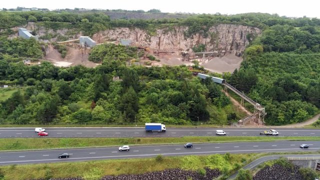 Aerial rising above North Wales expressway to CEMEX mining development site on lush greenery hillside
