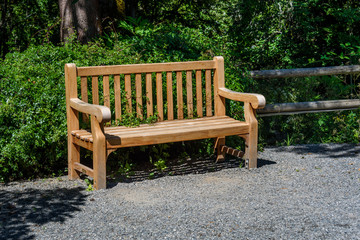 Fototapeta na wymiar Wooden bench in off a gravel path in a park, ready for a break 
