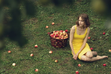 A young woman sits on the lawn next to a basket of apples.