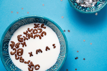 Top view of bowl with milk and chocolate alphabet cereals. Merry xmas text. Blue background