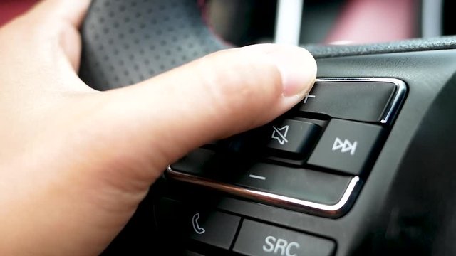 Close up of finger pressing the audio control buttons to increase or decrease the volume on the steering wheel when driving.