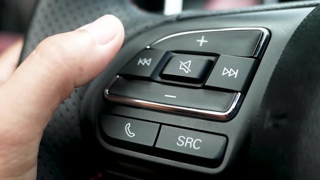 Close up of finger pressing the audio control buttons to increase or decrease the volume on the steering wheel when driving.