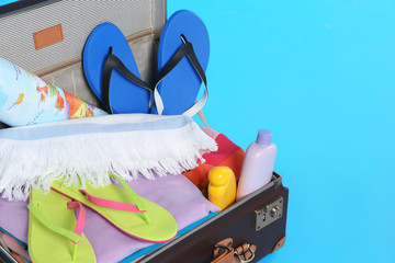 Open vintage suitcase with different beach objects packed for summer vacation on light blue...