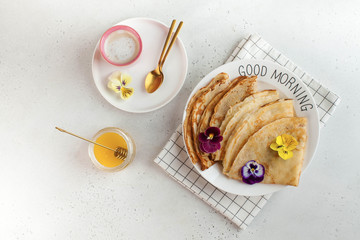 French crepes, pancakes decorated with flowers, a mug of cappuccino and honey. Concept of...