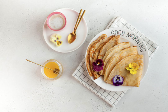 French crepes, pancakes decorated with flowers, a mug of cappuccino and honey. Concept of Breakfast, dessert. Copy space