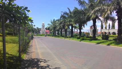 Obraz premium The entrance to a residential area with a palm tree in the middle. the road is made by the paving method