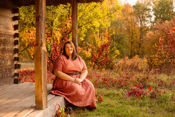 Beautiful and confident plus size model in red dress and brown boots  posing outdoors at autumn landscape with traditional russian architecture
