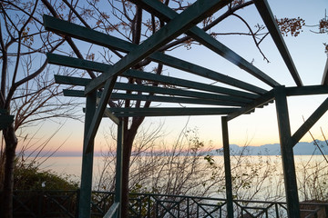 View of the gazebo with wooden slats, plant silhouettes and the sky in the background at sunset in the evening