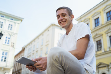 Young creative man sitting in a street and using tablet computer