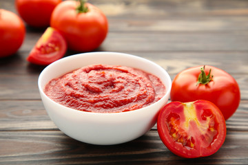 Tomato ketchup sauce in a bowl with tomatoes on brown. View from above.