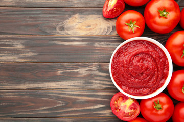 Tomato ketchup sauce in a bowl with tomatoes on brown. View from above.