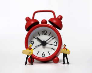 Miniature deliverymen holding parcels and a red alarm clock.
