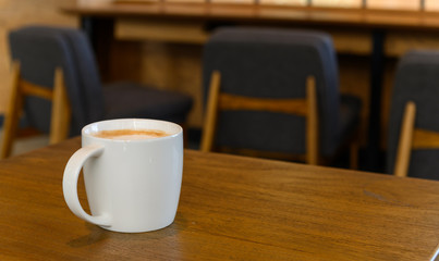 white coffee cup with hot cappuccino coffee on wooden table in coffee cafe. copy space for adding text