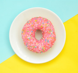 Pink glazes donut on white plate on pastel yellow turquoise background