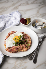 Norddeutscher Hamburger Labskaus mit Rindfleisch Corned Beef, Rote Beete, Kartoffeln, Saure Gurken, Spiegelei und Rollmops auf Teller