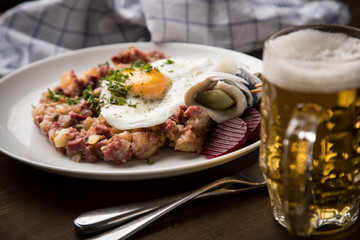 Norddeutscher Hamburger Labskaus mit Rindfleisch Corned Beef, Rote Beete, Kartoffeln, Saure Gurken, Spiegelei, Rollmops und Bier auf Holztisch