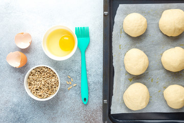 Pieces of raw dough on a pan, silicone brush, egg, seeds. Cooking homemade buns. Top view