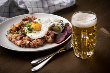 Norddeutscher Hamburger Labskaus mit Rindfleisch Corned Beef, Rote Beete, Kartoffeln, Saure Gurken, Spiegelei, Rollmops und Bier auf Holztisch