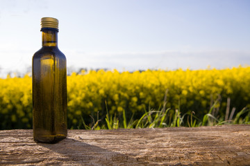 Rapeseed oil in bottles on white wooden table on background flowering rape field.