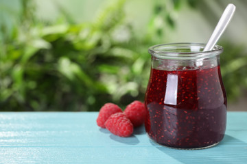 Delicious jam in glass jar and fresh raspberries on blue wooden table. Space for text