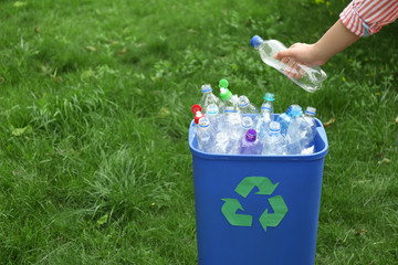 Woman throwing used bottle into trash bin outdoors, closeup. Plastic recycling