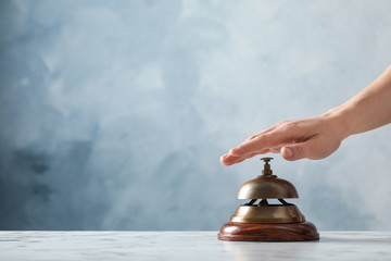 Man ringing hotel service bell at table on blue background, closeup. Space for text
