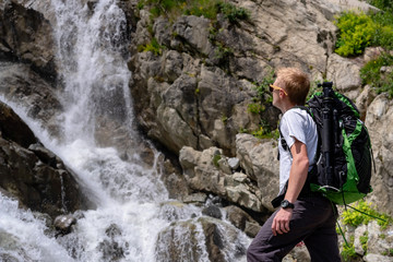 Naklejka na ściany i meble Man hiking with backpack looking at waterfall. Portrait of male adult back standing outdoor.