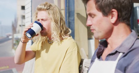 Two Caucasian male surfboard makers sitting on a bench and drinking takeaway coffee - Powered by Adobe