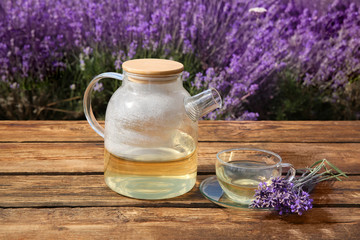 Obraz na płótnie Canvas Tasty herbal tea and fresh lavender flowers on wooden table in field